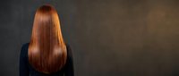 Young woman with long straight red hair from behind against dark background showcasing healthy shiny hair care and beauty treatment results.