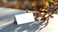 Blank white folded card with autumn golden leaves casting shadows on light surface, minimalist composition for seasonal greetings or announcements.