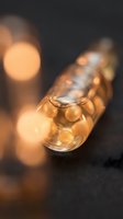 Golden oil droplets in glass pipette with warm bokeh lighting on dark background, suitable for cosmetics, skincare, and wellness product marketing.