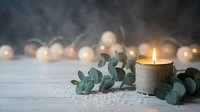 Burning candle with eucalyptus leaves on wooden surface creating peaceful spa atmosphere with warm bokeh lights in background for relaxation.