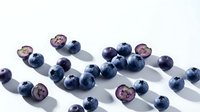 Assorted fresh blueberries scattered on white surface with shadows, suitable for food photography, culinary design, and healthy eating content.