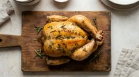 Golden roasted whole chicken with herbs on rustic wooden cutting board, ready to serve for family dinner or holiday meal preparation.