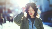 Young Asian woman with headphones listening to music on city street with warm sunlight and urban bokeh background for lifestyle and technology concepts.