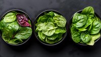 Fresh green spinach leaves in black bowls arranged in row on dark background, top view. Healthy organic salad ingredients for cooking and nutrition.