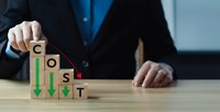 Businessman arranging wooden blocks spelling COST with downward arrows showing expense reduction and budget optimization strategies in corporate office.