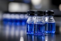 Glass vials with bright blue liquid in laboratory setting, shallow depth of field creates soft background blur, medical research concept for healthcare industry.