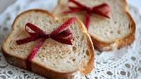 Slices of white bread shaped as hearts, tied with delicate red ribbon bows, arranged on lace doily for romantic breakfast or Valentine's Day celebration.