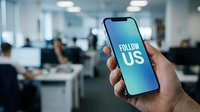 Hand holding smartphone with Follow Us text on screen in modern office, social media marketing concept for business growth.