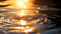 Golden water drop creating concentric ripples on dark liquid surface with sunlight bokeh reflections, capturing moment of impact in macro photography.