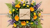 Kraft paper gift box surrounded by wildflower wreath with orange poppies, purple lavender and yellow blooms on neutral background for celebrations.