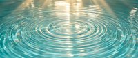 Tranquil water ripples create perfect concentric circles with golden sunlight reflections on turquoise blue surface for meditation and wellness concepts.