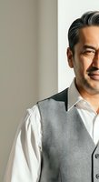 Middle-aged man with dark hair and facial hair wearing white dress shirt and gray vest against neutral background, suitable for corporate, business, and professional portraits.