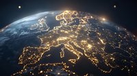 Night view of Europe from space showing illuminated cities and countries with glowing light clusters across continental landmass against dark background.