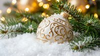 Cream and gold ornamental bauble nestled in snow among evergreen branches and warm golden lights, suitable for holiday and seasonal marketing materials.