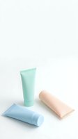 Colorful cosmetic tubes in mint green, soft blue and peach pink arranged on clean white background for skincare and beauty product mockups.