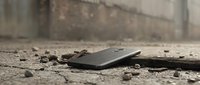 Broken smartphone with cracked screen lying on concrete ground surrounded by debris and rubble in urban environment for technology damage concept.