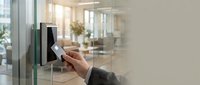 Professional using keycard access system at modern office entrance with glass doors and contemporary interior design for workplace security.