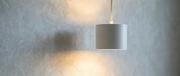 Minimalist pendant lamp with cylindrical shade casting warm light on textured gray wall, suitable for modern interior design and home decor projects.