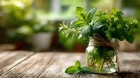 Fresh mint and herbs in glass jar on rustic wooden table with soft blurred garden background, ideal for culinary, aromatherapy, or natural home decor.
