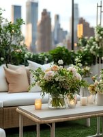 Elegant rooftop terrace setting with fresh floral arrangements and glowing candles against urban skyline backdrop, featuring comfortable outdoor furniture and lush greenery.