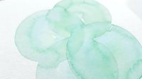 Soft mint green watercolor paint strokes creating organic flowing shapes on white paper background for artistic design projects and creative layouts.
