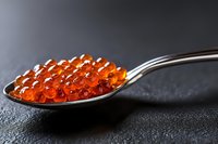 Red caviar on silver spoon against dark background. Luxury gourmet seafood delicacy for fine dining and culinary presentations.