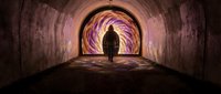 Silhouette of person walking through illuminated tunnel with vibrant purple and orange light effects creating mystical atmosphere for spiritual concepts.