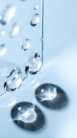 Clear water droplets falling and creating ripples on pristine surface with reflective bubbles for skincare cosmetics and hydration concepts.