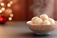 Steaming rice balls in traditional Asian bowl with geometric pattern against blurred festive bokeh lights and red ornament background.