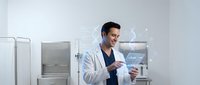 Young Asian male scientist in white lab coat holding tablet computer in modern sterile laboratory with equipment for research and medical analysis.