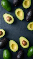 Fresh ripe avocados arranged on dark slate background, whole and halved fruits showing creamy flesh and pits for healthy cooking and nutrition content.