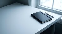 Minimalist workspace with black leather notebook and pen on clean white desk near window for professional office productivity and business planning.