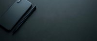 Black smartphone and stylus pen on dark textured surface, minimalist tech workspace setup for mobile app development, design, and digital content creation projects.