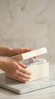Female hands opening white gift box with tissue paper on marble surface. Elegant present unboxing moment for special occasions and celebrations.