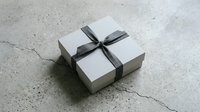 White gift box with elegant black ribbon bow on concrete floor for special occasions and celebrations.