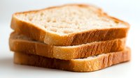 Fresh sliced white bread stacked in layers showing soft texture and golden crust, photographed with selective focus on bright background for food packaging.