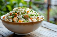 Fresh vegetable fried rice with carrots, peas, mushrooms and herbs served in white ceramic bowl on rustic wooden table with natural lighting and blurred background.