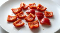 Fresh red bell pepper slices arranged on white plate, raw vegetable pieces ready for cooking, healthy ingredient preparation for salads and meals.
