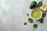 Fresh avocado sauce with baby spinach leaves and ripe avocado on light gray concrete background, top view with copy space for menu design.
