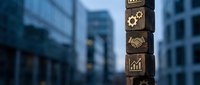Stacked wooden blocks with business icons including gears, chart, and dollar sign symbolizing corporate growth and financial success in modern city environment.