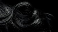 Flowing dark hair strands creating elegant waves and curls against black background for beauty and haircare concepts.