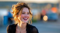 Young woman with tousled hair and bright smile laughing outdoors during golden hour, with soft bokeh background creating warm atmosphere.