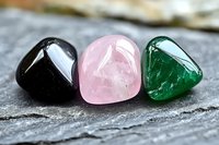 Three polished gemstones in black, pink and green colors arranged on textured stone surface for jewelry making, crystal healing and decorative purposes.