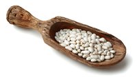 Rustic wooden scoop filled with white navy beans on white background, perfect for cooking, nutrition, and healthy eating concepts.