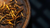 Dried golden tea leaves in rustic ceramic bowl, close-up shot showcasing texture and color for beverage, wellness, and culinary design projects.