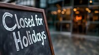 Handwritten chalk text on blackboard saying closed for holidays with blurred storefront and bokeh lights in background, business closure notice.