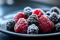 Fresh raspberries and blackberries dusted with powdered sugar on dark plate, macro food photography with selective focus and soft natural lighting.