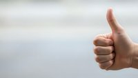Hand showing thumbs up gesture against blurred background expressing approval, success and positive feedback for business and communication concepts.