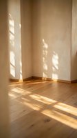 Empty room corner with warm sunlight streaming through window creating geometric shadows on white walls and natural wood flooring for interior design concepts.