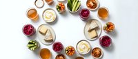 Colorful assortment of healthy dips, sauces and spreads in small bowls arranged in circle on white background for party appetizers and snacking.